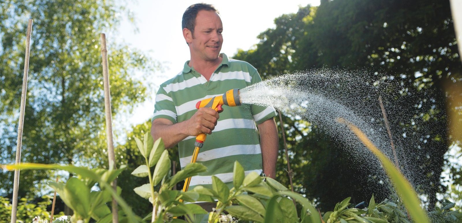 A gardener watering plants with a Hozelock spray gun